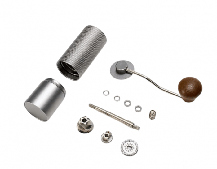 Zerlegte manuelle Kaffeemühle mit Edelstahlgehäuse, Mahlwerk, Kurbel mit Holzgriff und Einzelteilen auf weißem Hintergrund