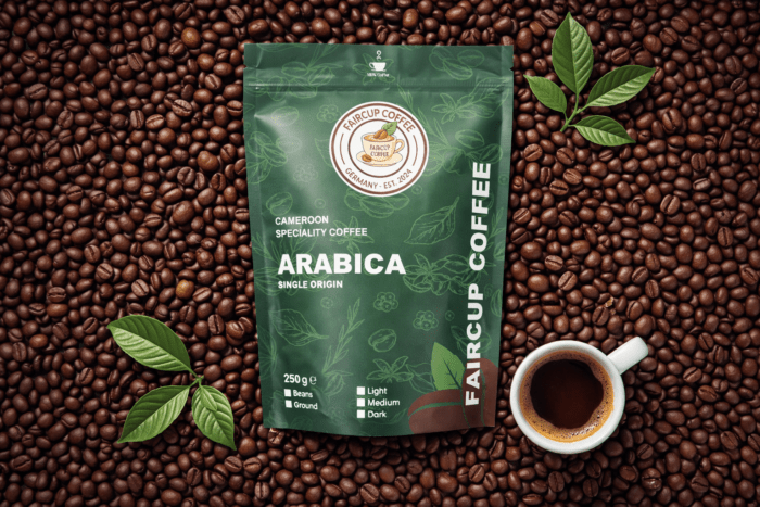 Grüne Packung mit Single Origin Arabica Kaffee aus Kamerun auf Kaffeebohnen, daneben Tasse und Kaffeeblätter