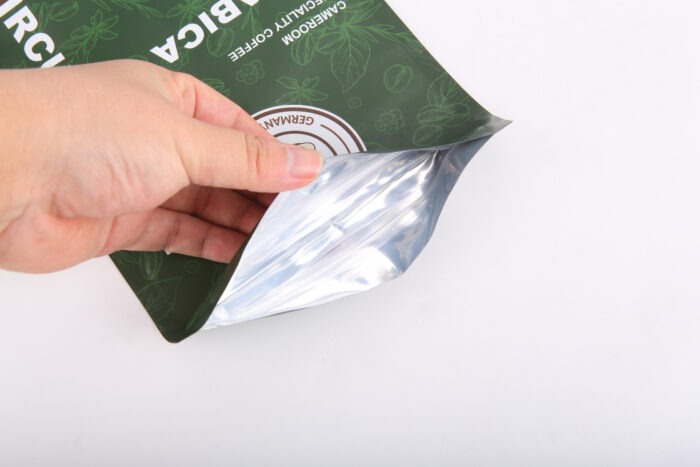 Hand öffnet grüne Kaffeepackung mit durchsichtiger Innenseite, auf der Verpackung steht Arabica und Cameroom