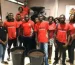 Gruppe von Menschen in roten T-Shirts steht hinter großen Behältern mit Kaffeebohnen in einem Innenraum